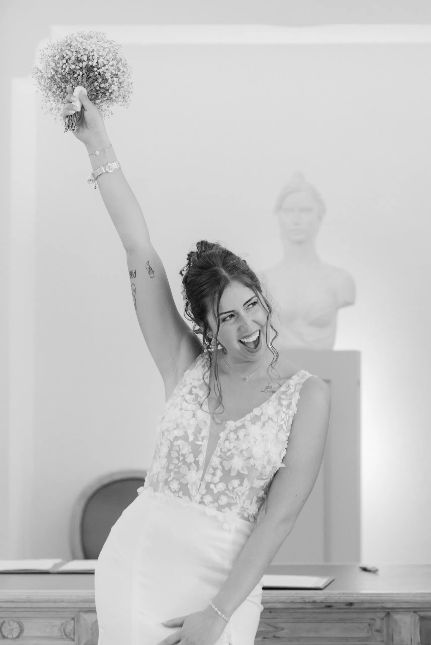 La mariée lève son bouquet en riant, en noir et blanc