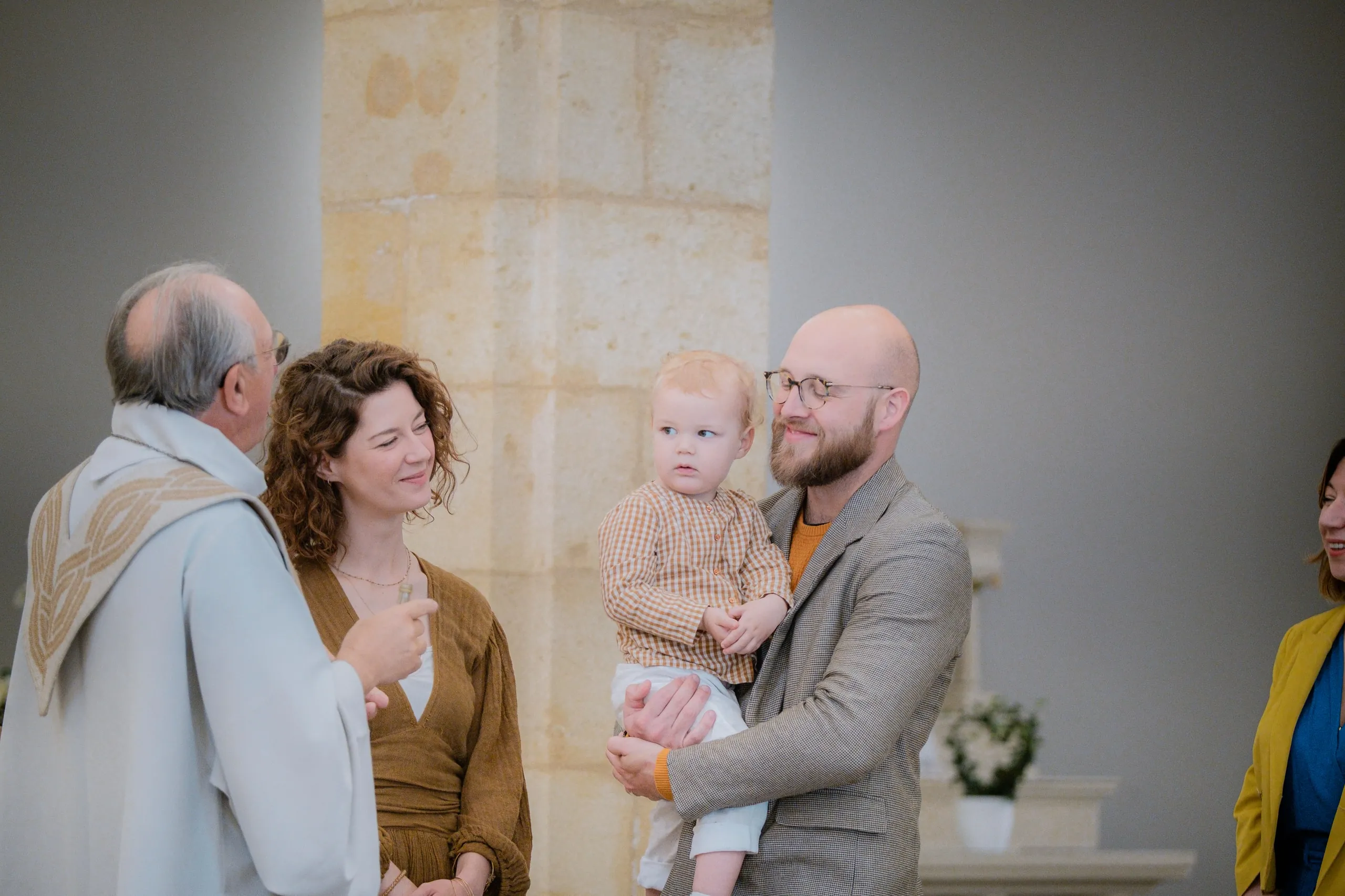 Le prêtre s'adresse à la mère qui sourit, à côté du père qui regarde avec tendresse son petit garçon dans ses bras