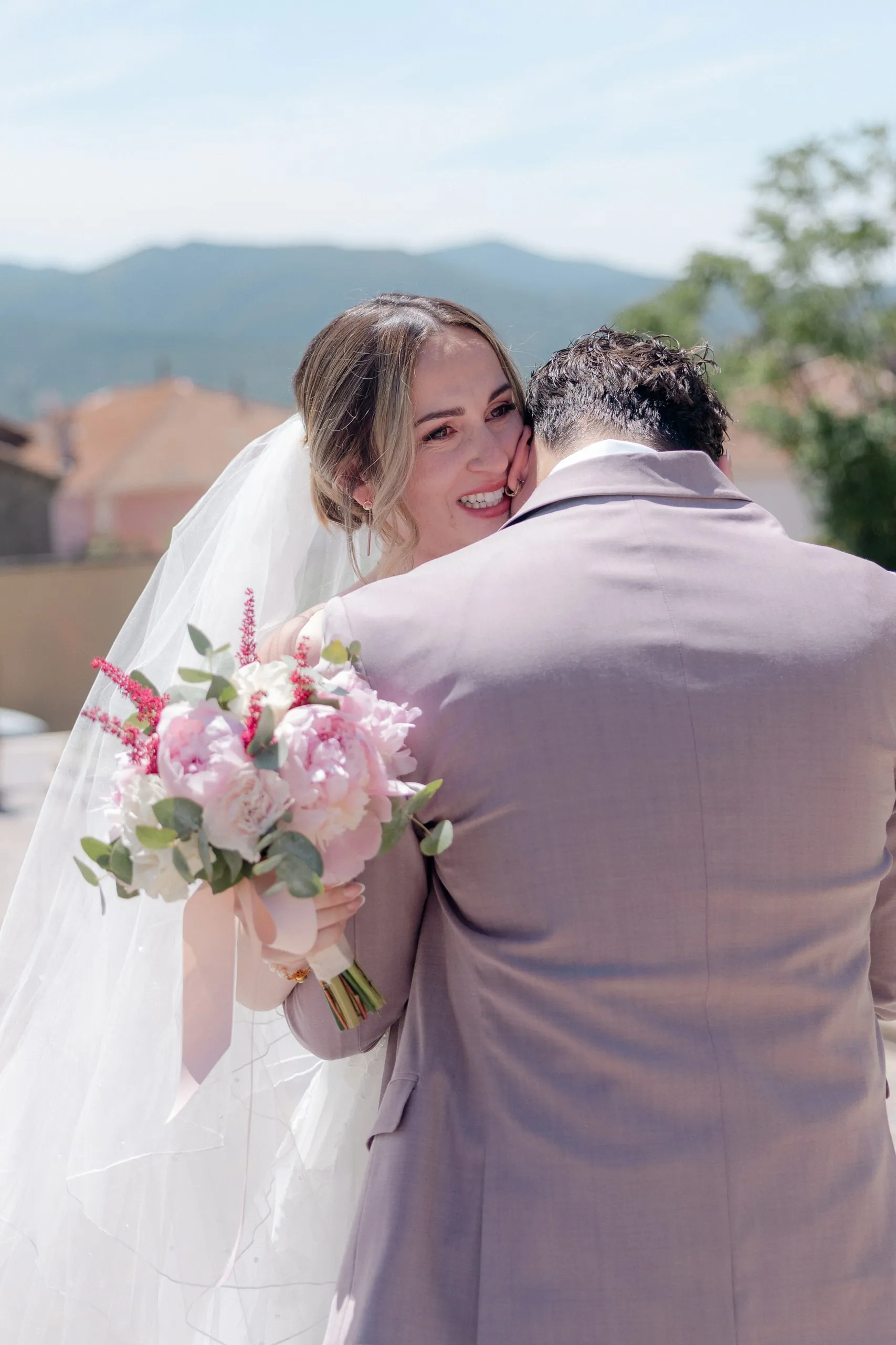 La mariée serre son mari dans ses bras, son bouquet à la main, face aux collines